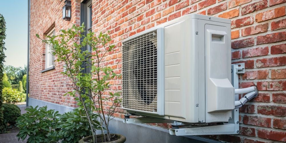 Modern outdoor heat pump unit mounted on the exterior brick wall of a home